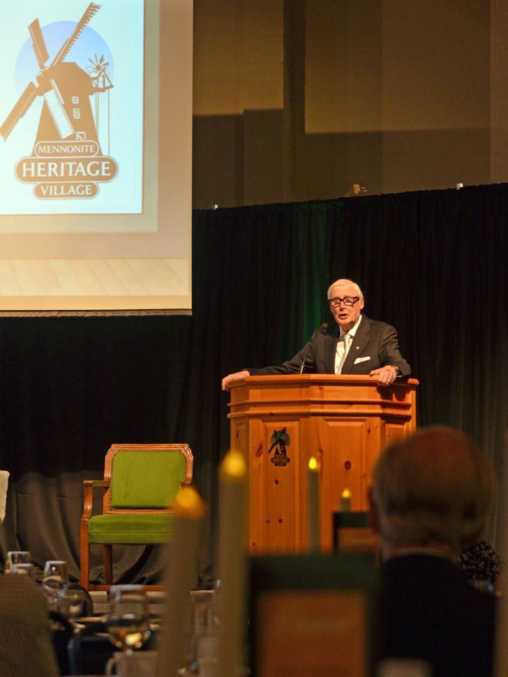 The Honourable Jake Epp speaking to guests at the MHV Gala, standing beside the chair he occupied while in Ottawa as MP for Provencher.